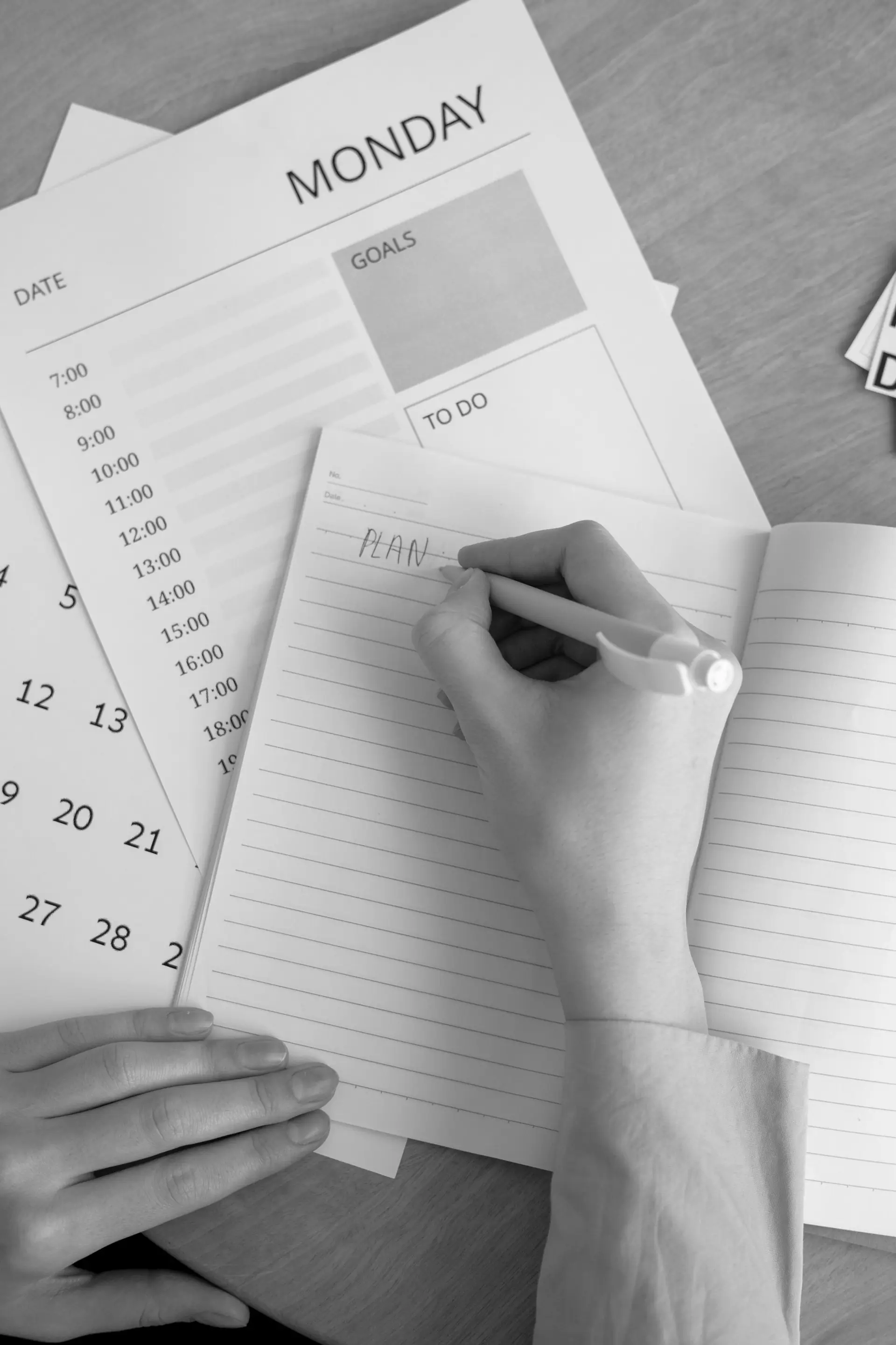 Eine Hand notiert in einem Notizbuch einen Plan, daneben ein Wochenkalender