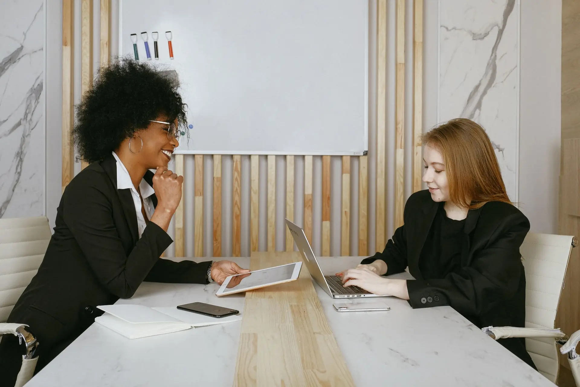 Zwei Kolleginnen besprechen an einem Tisch in einem modernen Büro Abläufe und Zuständigkeiten