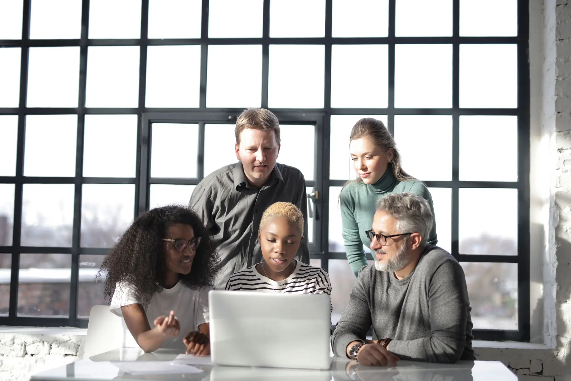 Ein kleines Team bespricht vor einer grossen Fensterfront gemeinsam die nächsten Schritte am Laptop